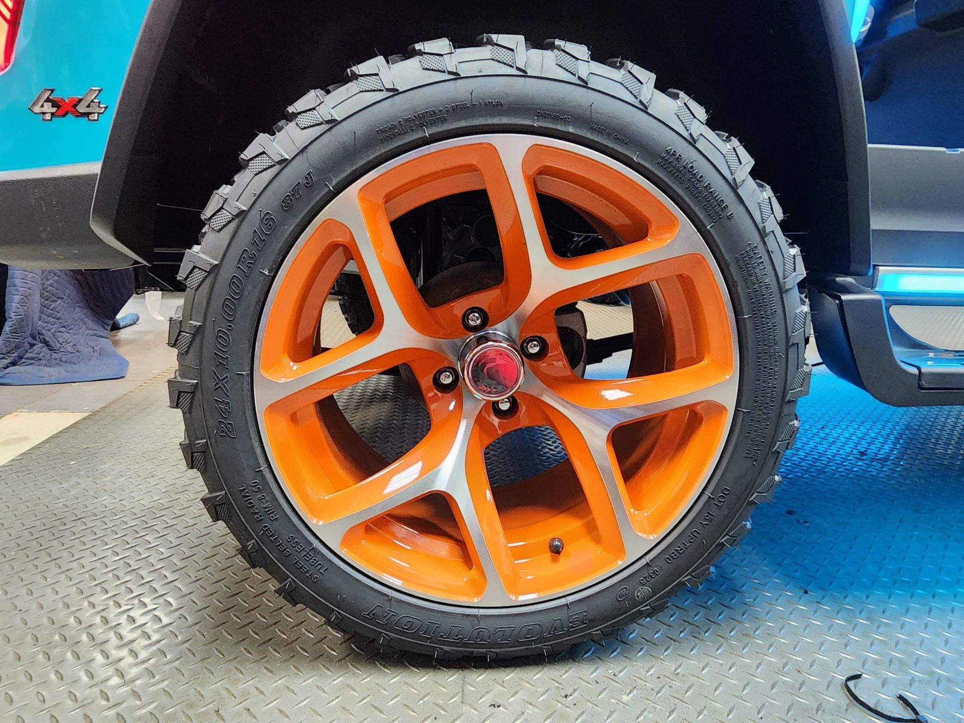 Close-up of a child's toy car wheel with an orange and silver rim and a black tire.