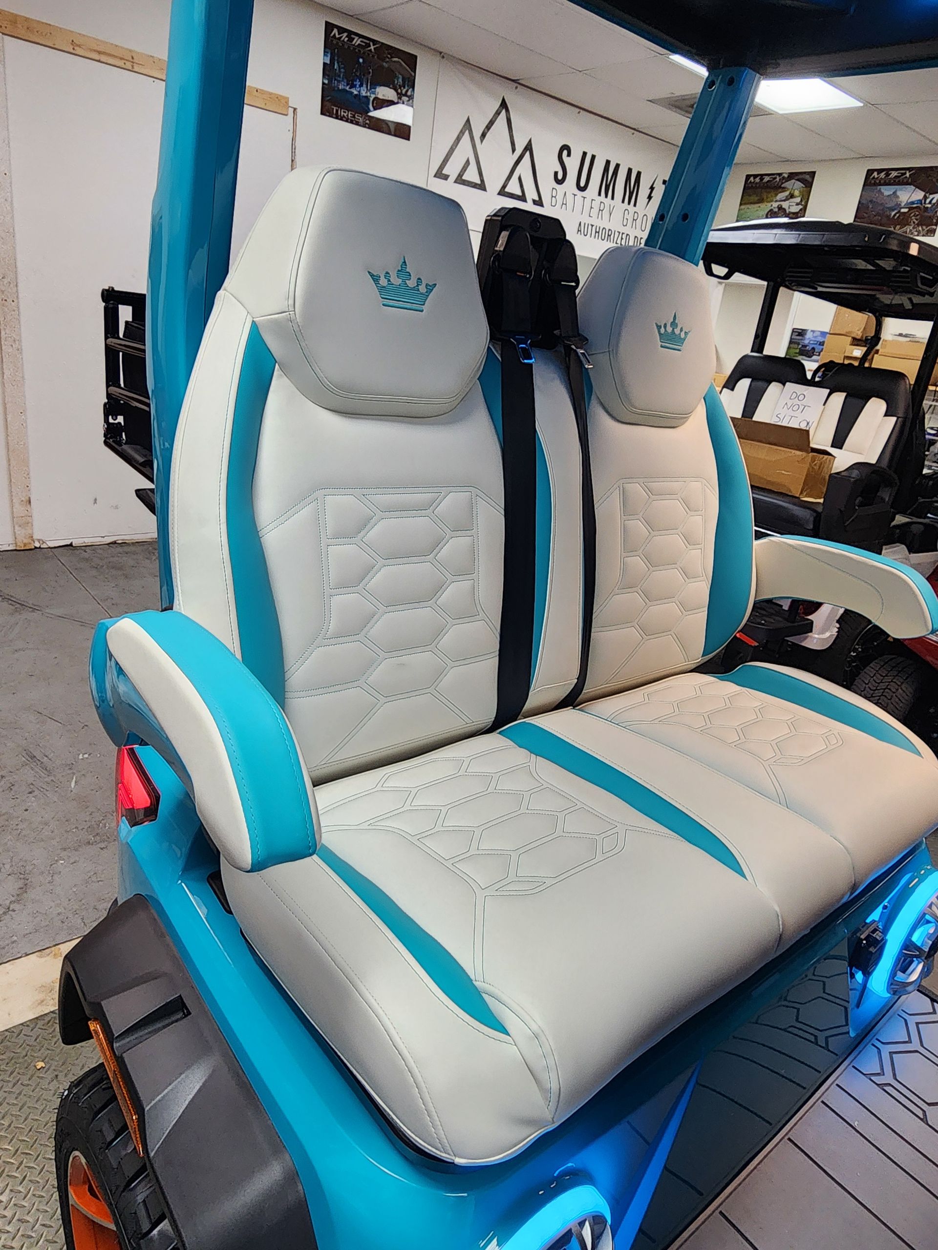 Custom golf cart seat, white with teal accents, diamond stitching, and headrests, lit with blue lights.
