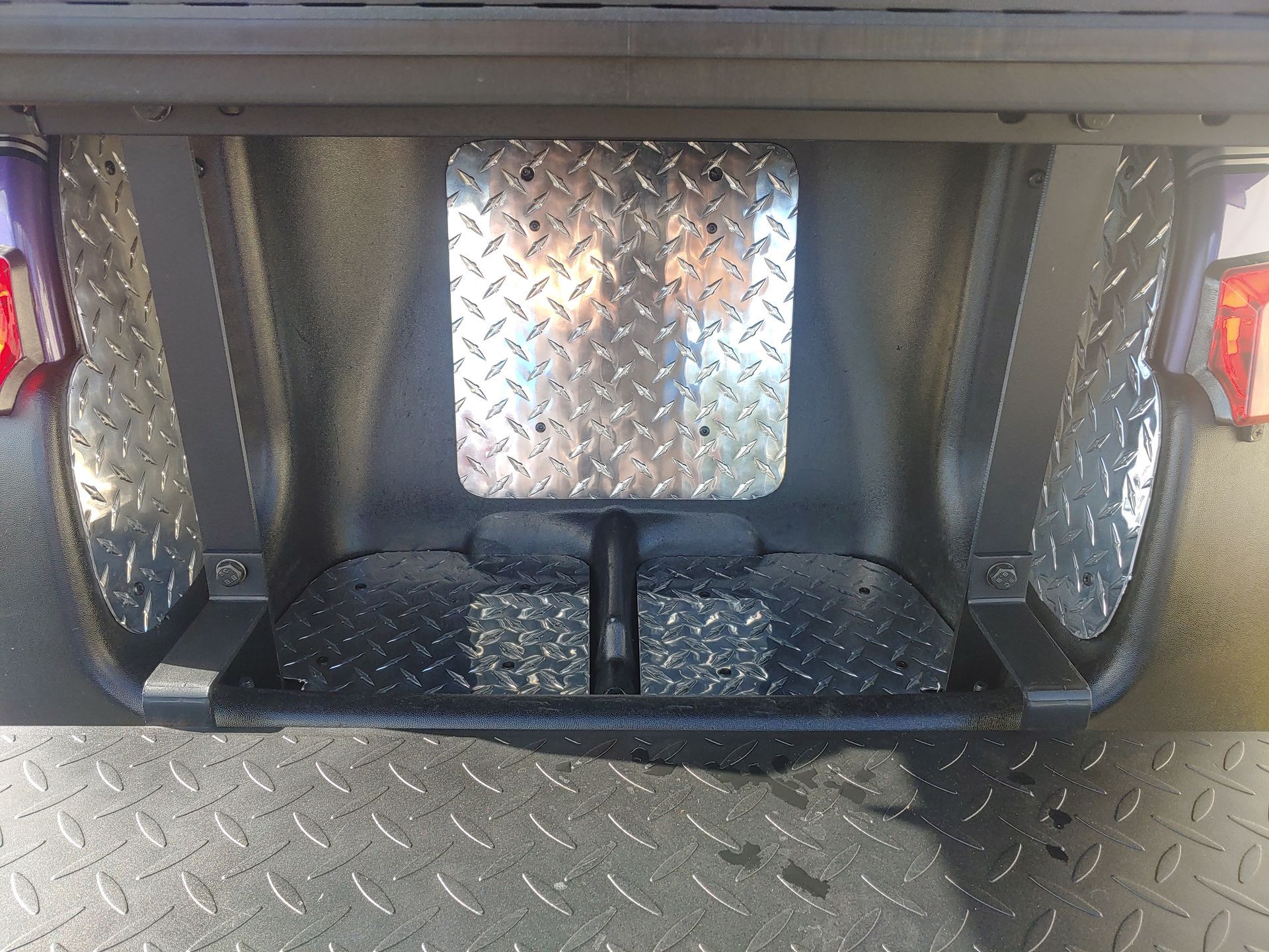 Rear of a vehicle with diamond plate metal features, including bumper and license plate mount.
