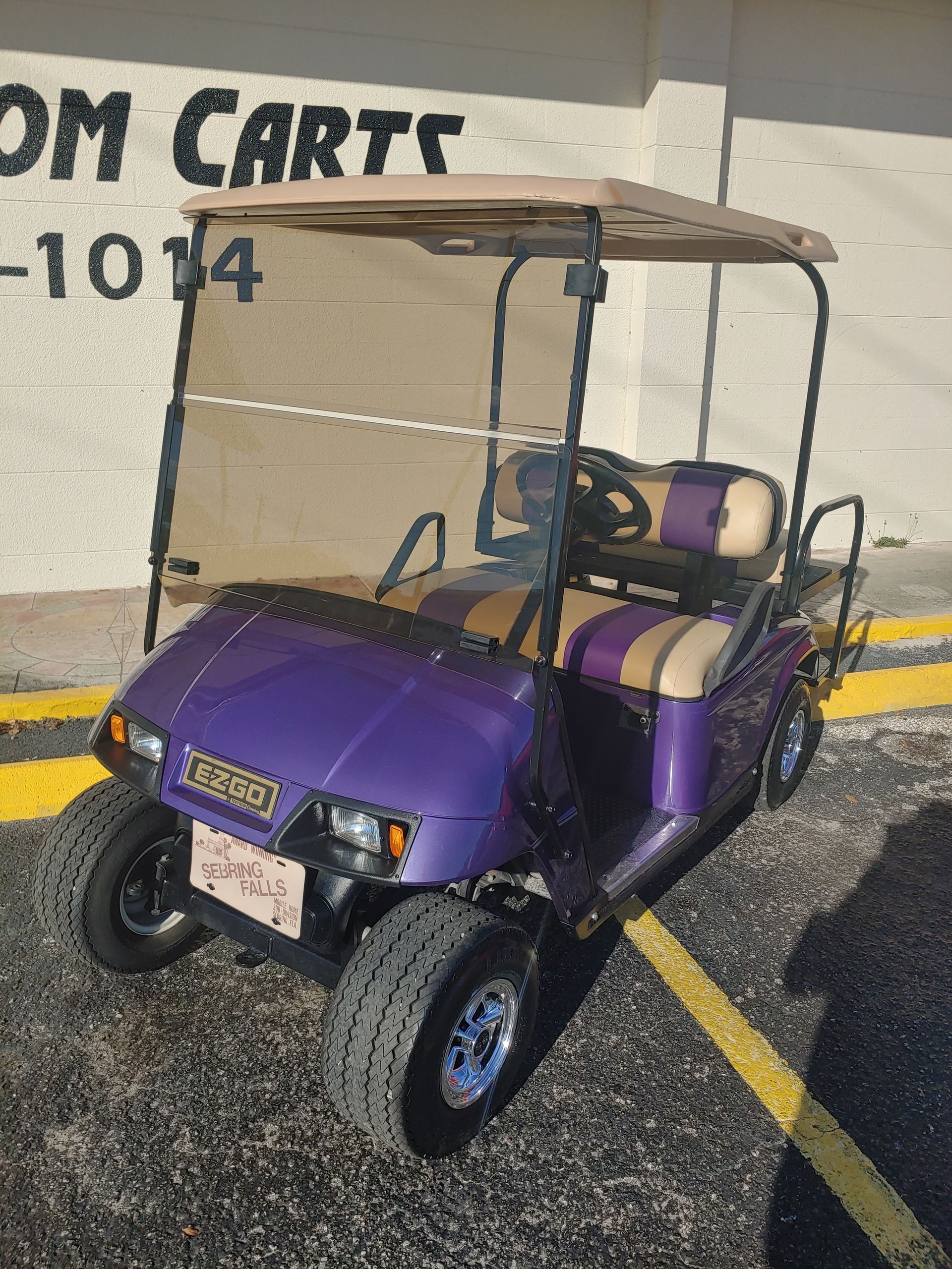 Purple and tan golf cart parked outside, with a tan roof and tinted windshield.