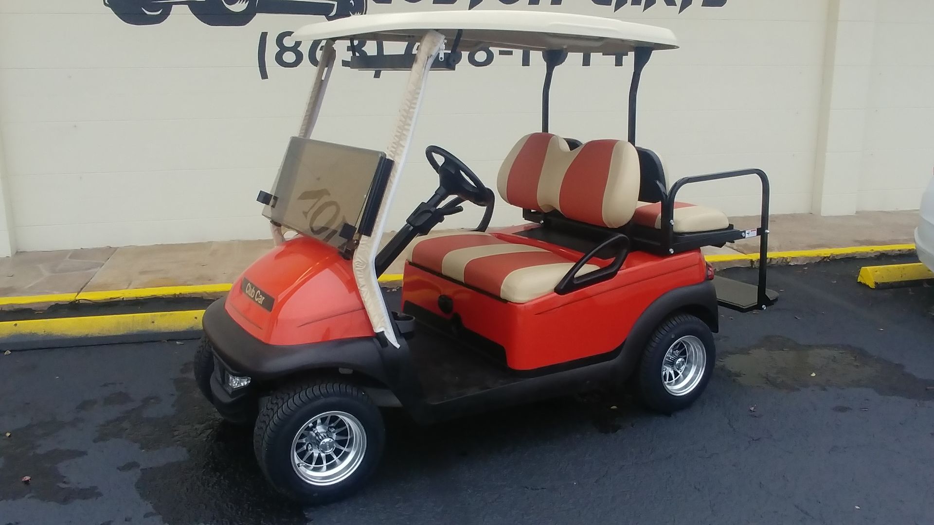 Red and tan golf cart parked on asphalt, near a building.