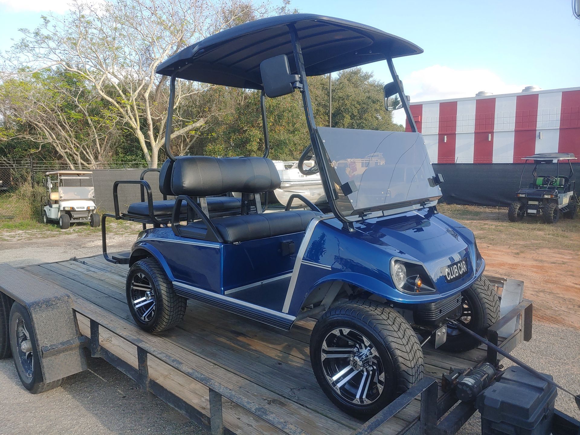 Blue golf cart on a trailer, black roof, silver accents, parked outdoors.