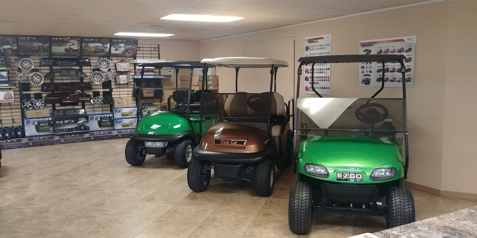 Three golf carts on display inside a showroom. Two are green, one is brown. Parts and accessories on shelves in background.