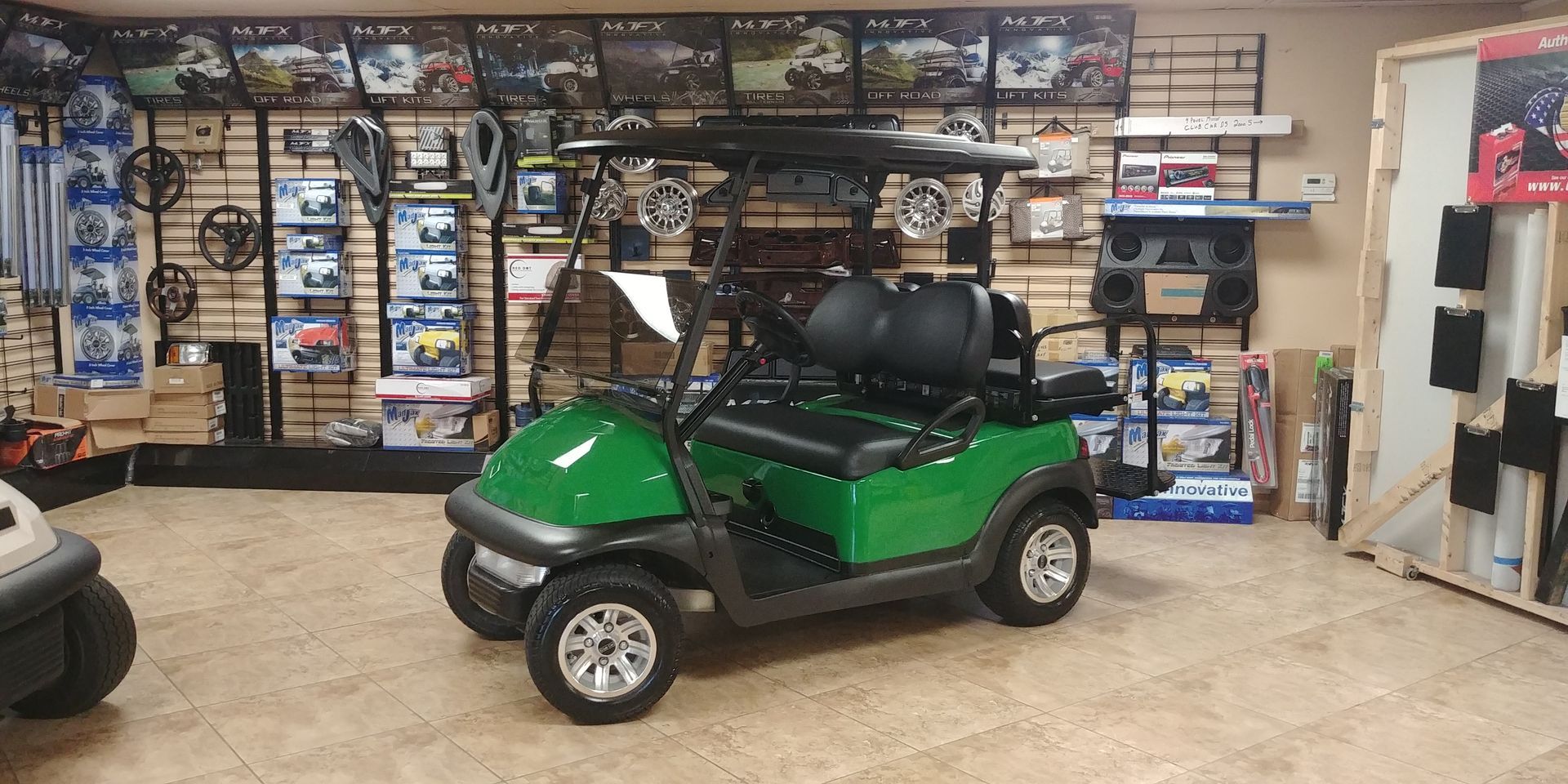 Green golf cart in a showroom with accessories on display.