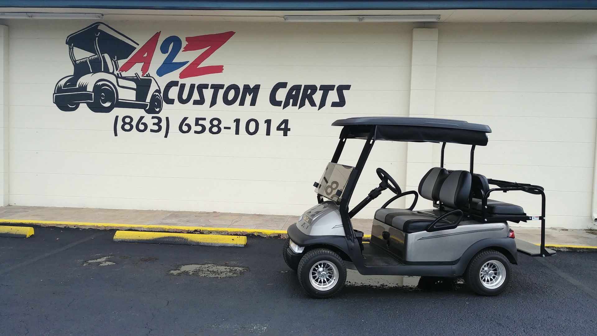 A silver golf cart parked in front of A2Z Custom Carts storefront with their logo and phone number painted on the wall.