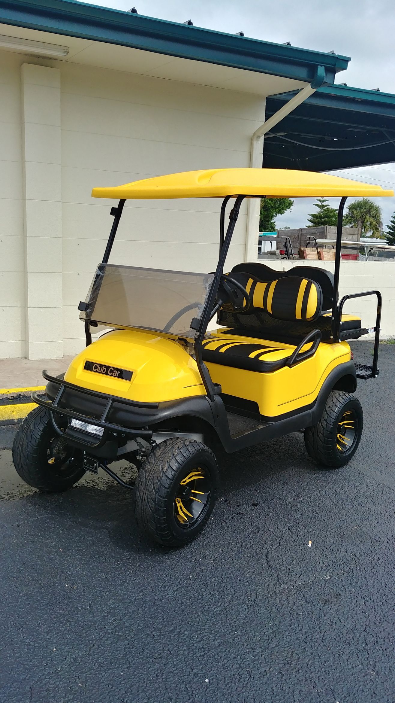 Yellow and black golf cart with canopy parked on pavement.