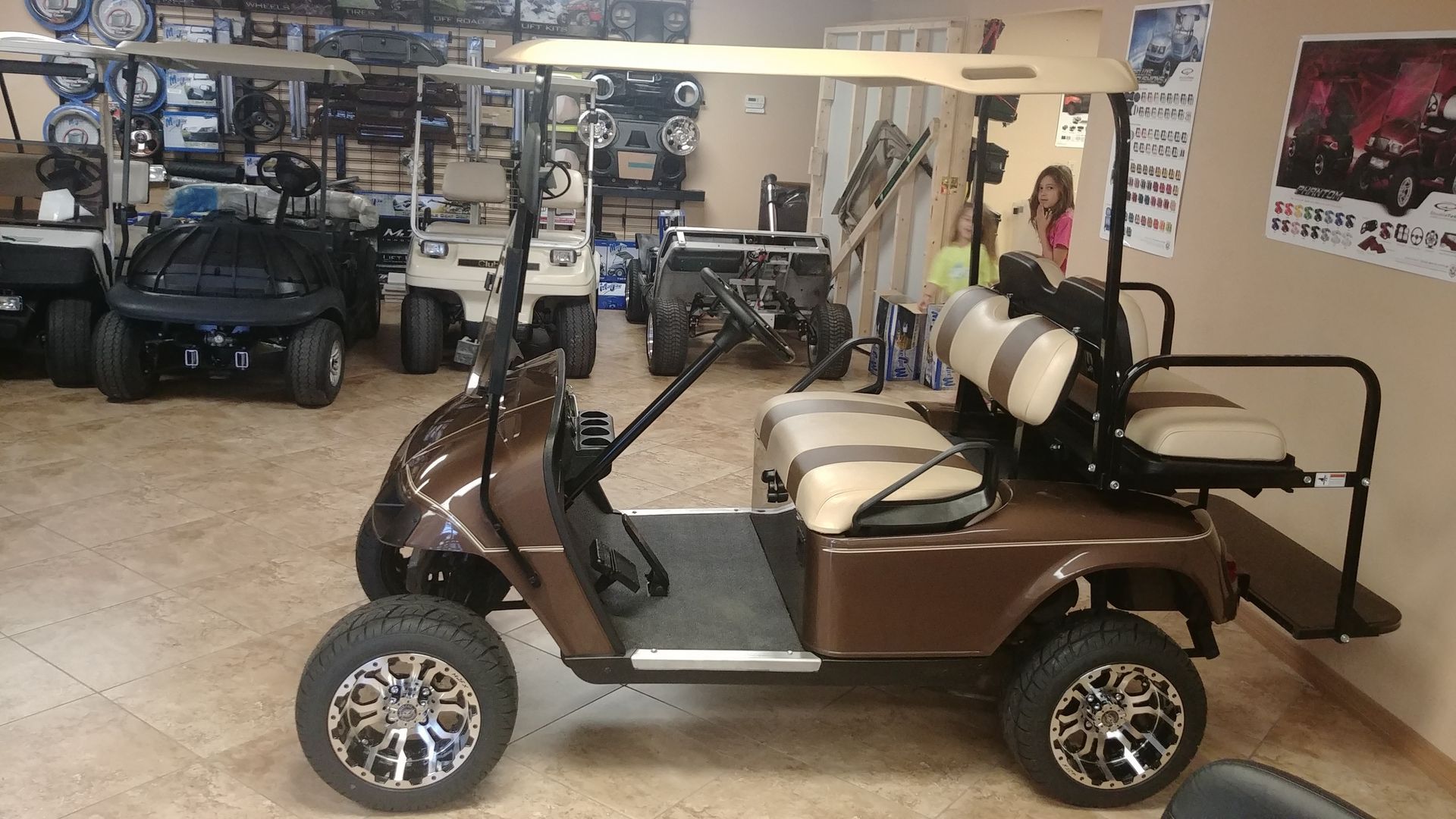 Brown golf cart with tan seats and large wheels in a showroom, other carts in background.