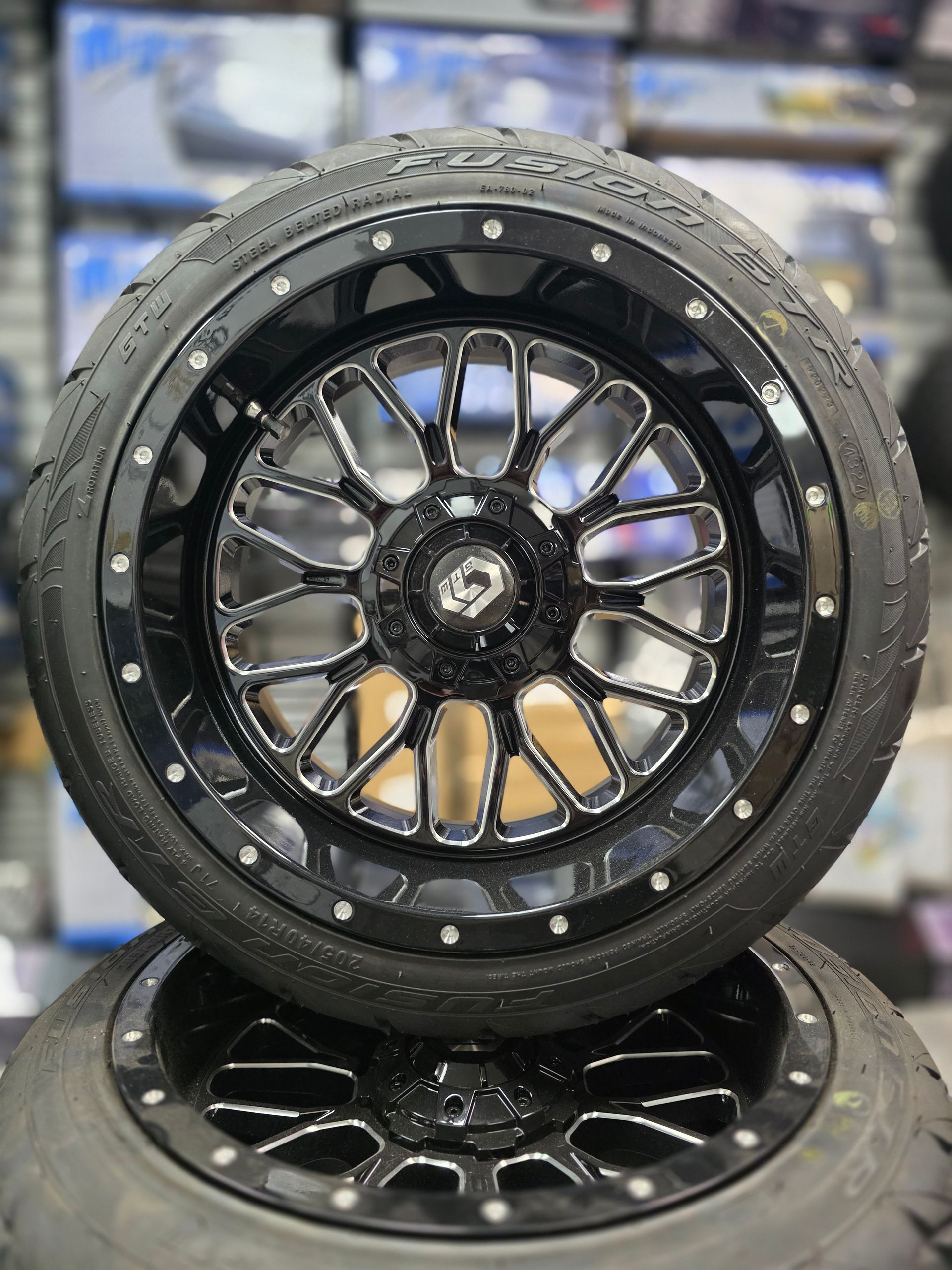 A stack of two black and chrome custom automotive wheels with tires, displayed in a retail or showroom setting.