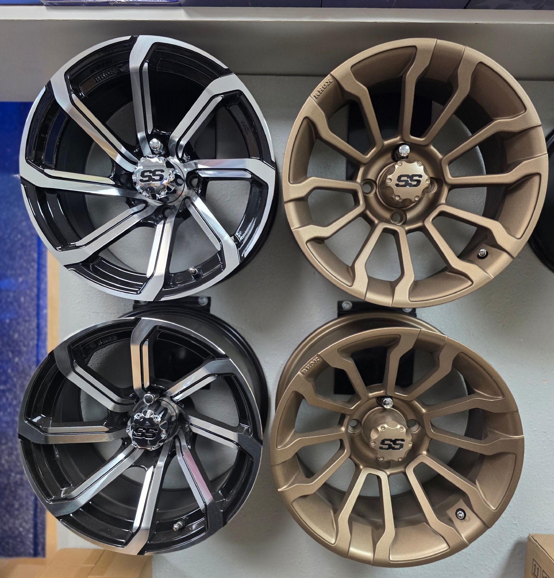 Four golf cart wheels mounted on a wall: two silver and black wheels on the left, and two bronze wheels on the right.