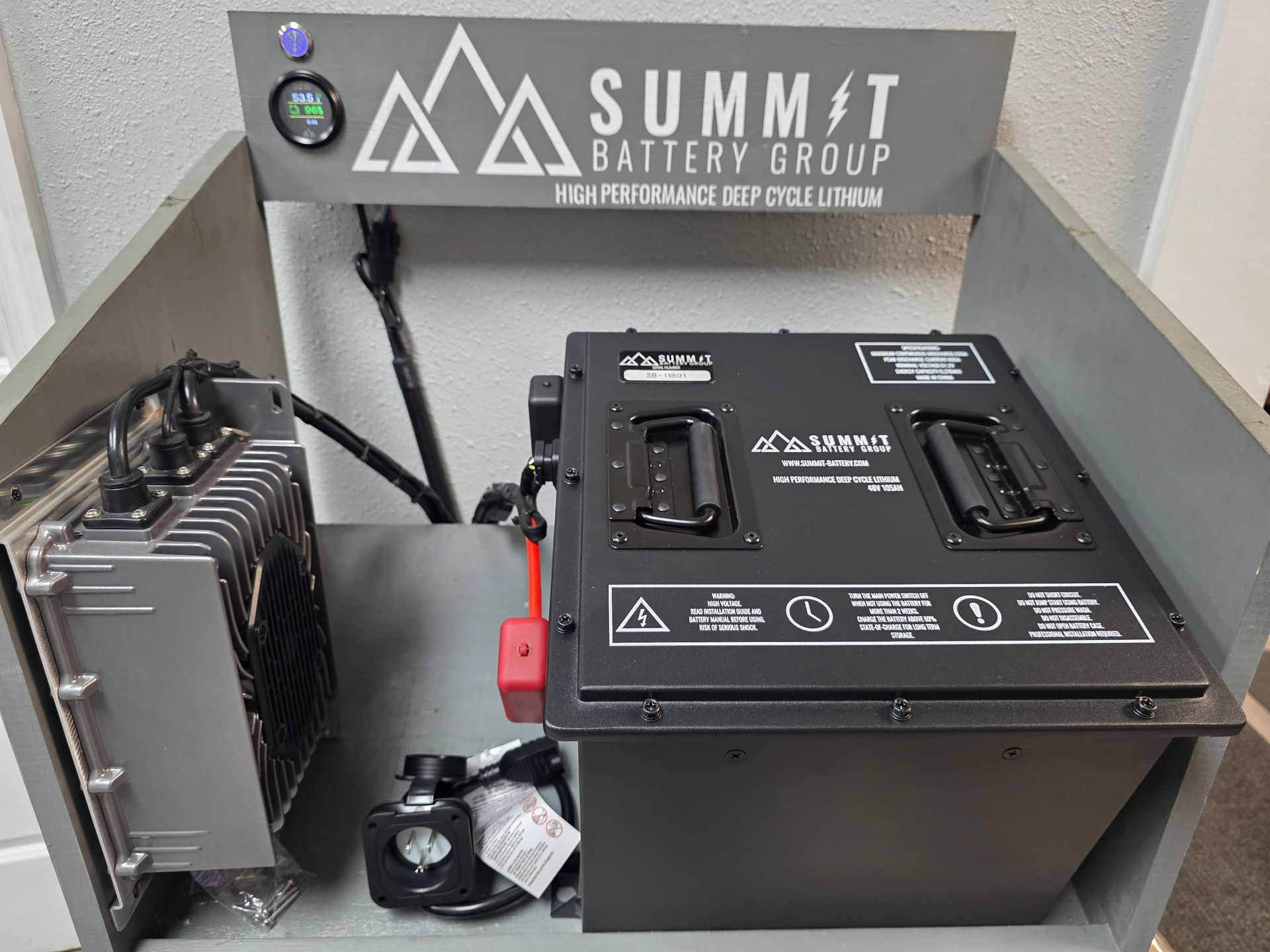 Battery charging setup with two black battery units and a metal power supply against a Summit Switch Group sign.