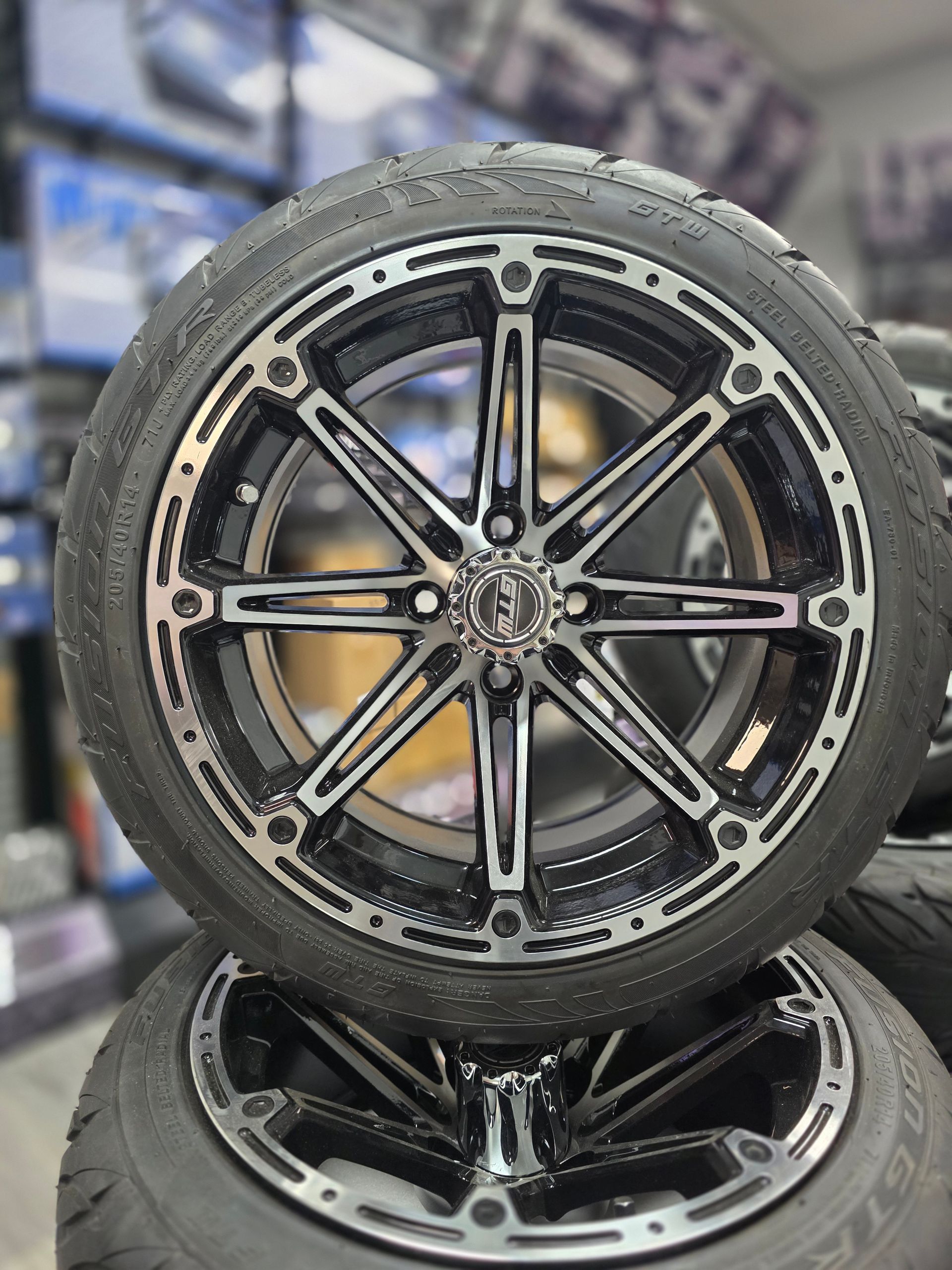 A black and silver aftermarket vehicle wheel with a multi-spoke design, mounted on a tire in a retail shop.