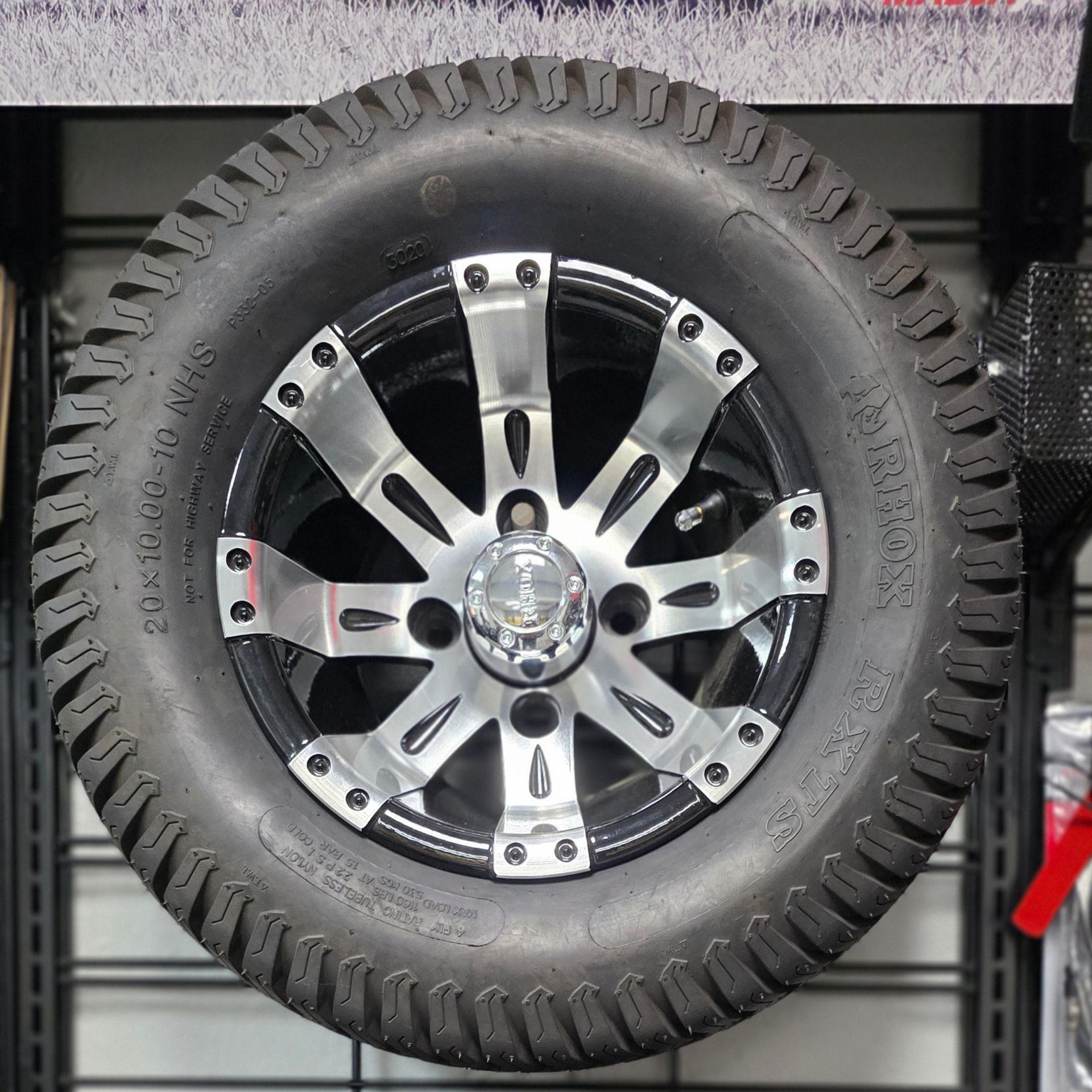 Black-and-silver off-road tire and wheel mounted on a display wall