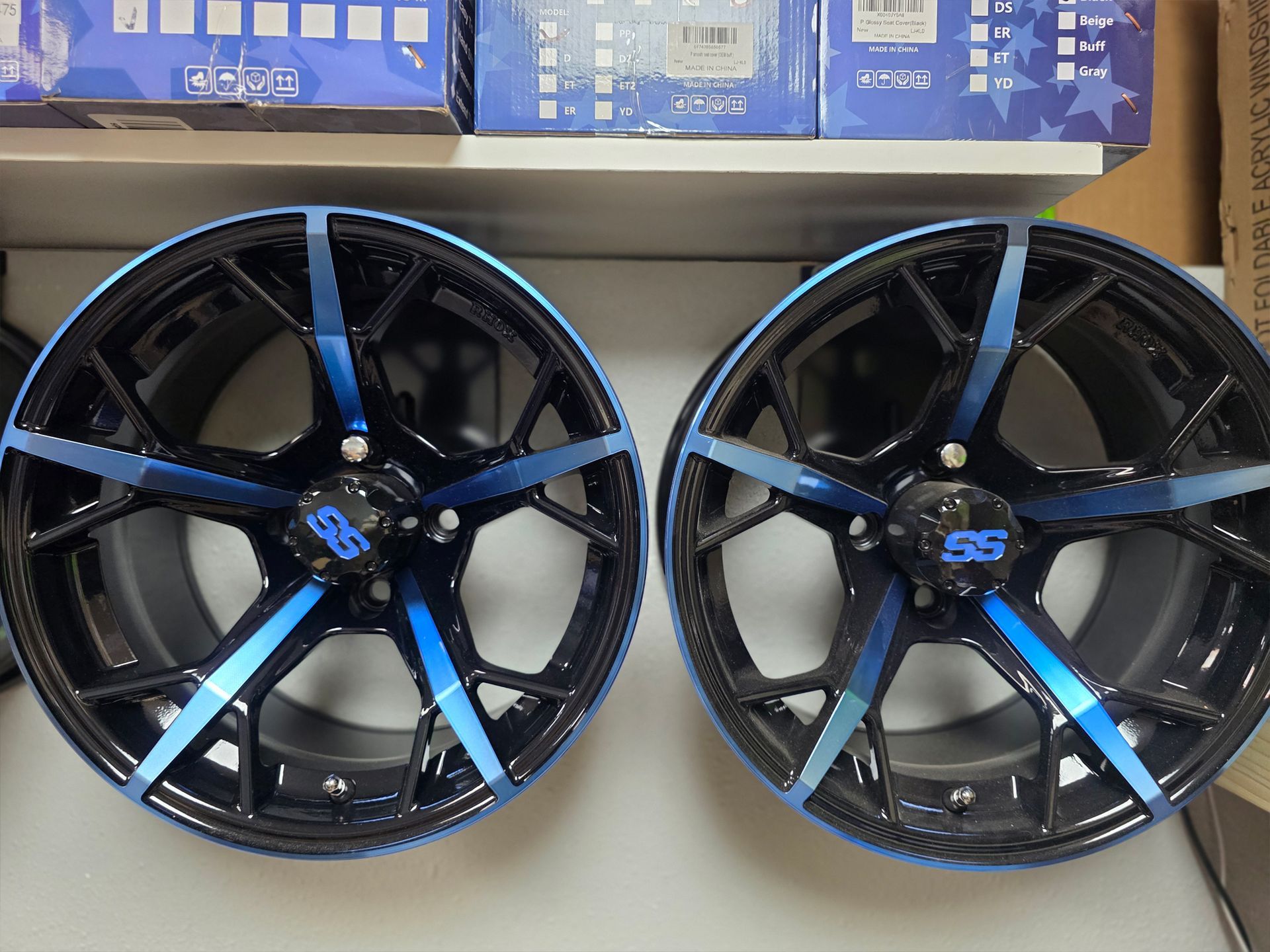 Two black-and-blue alloy wheels displayed side by side in a cardboard box