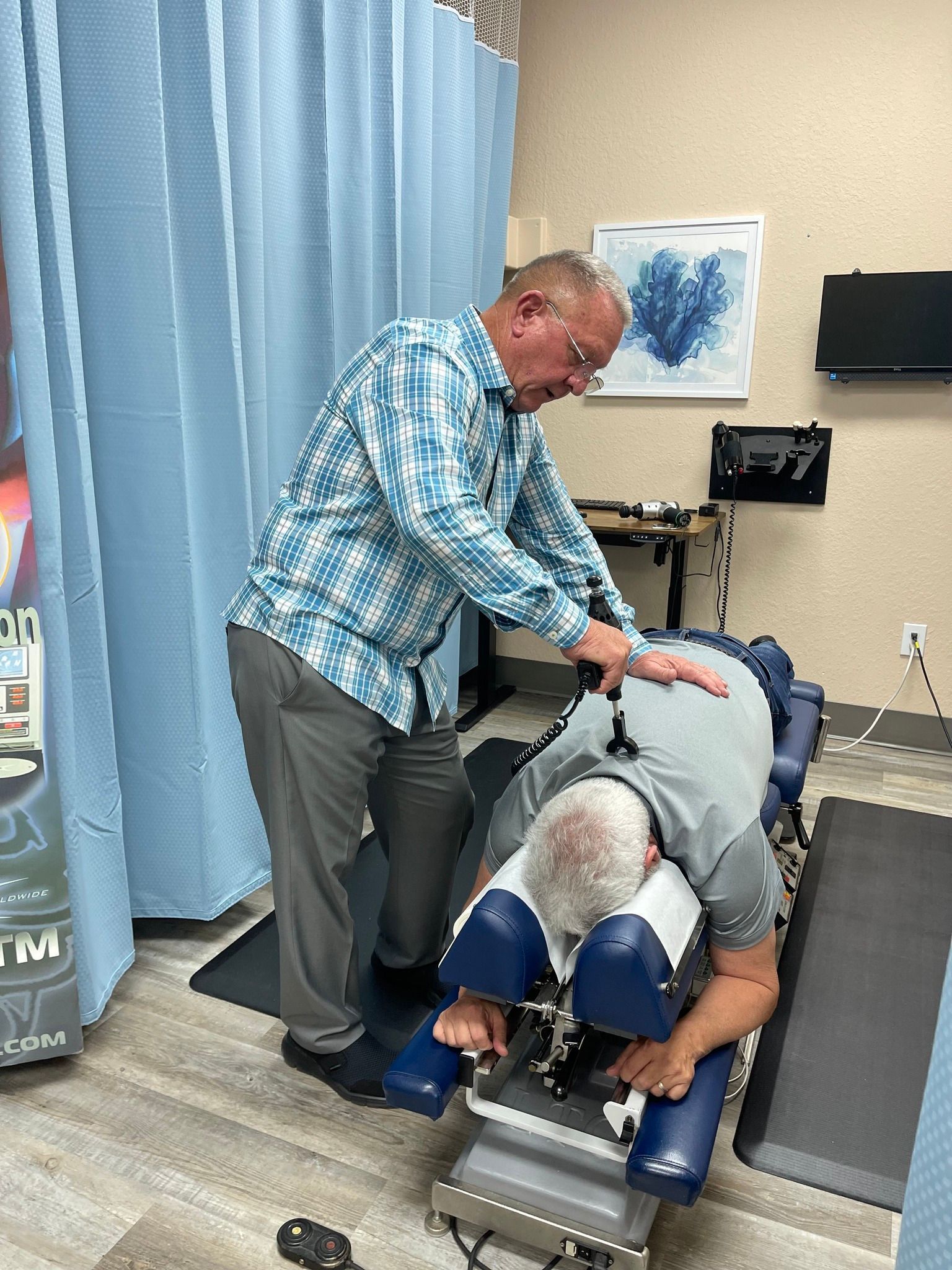 A chiropractor adjusts a patient's back. The patient lies face down on a padded table, while the chiropractor presses down with hands.