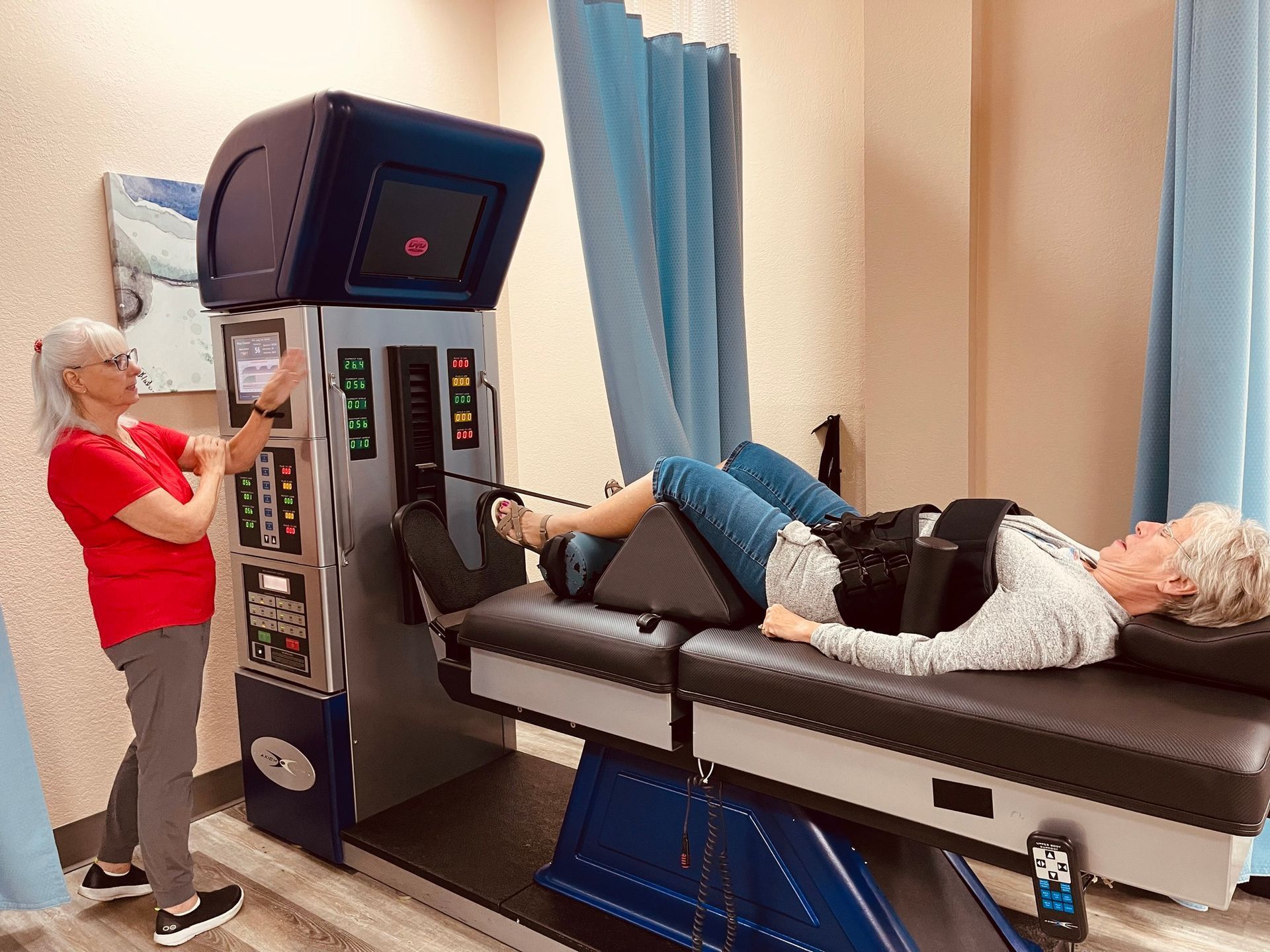A woman lies on a decompression therapy table, while another woman adjusts the machine's controls in a medical office.
