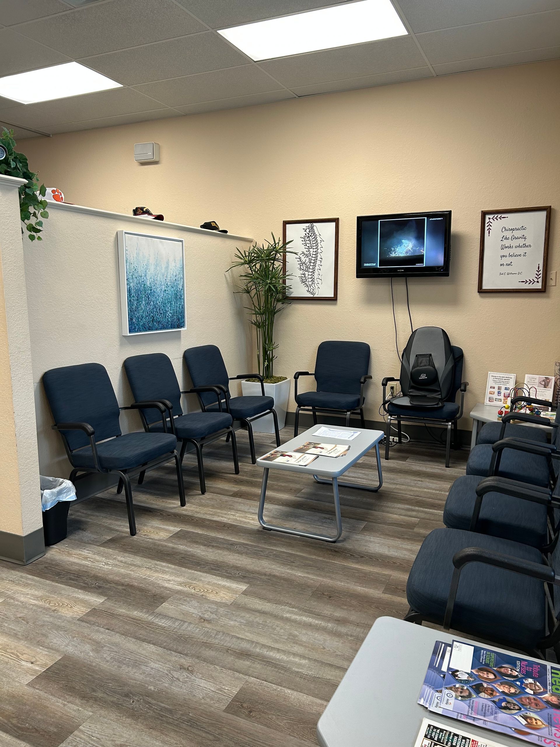 A waiting room with blue chairs , a coffee table , and a flat screen tv.