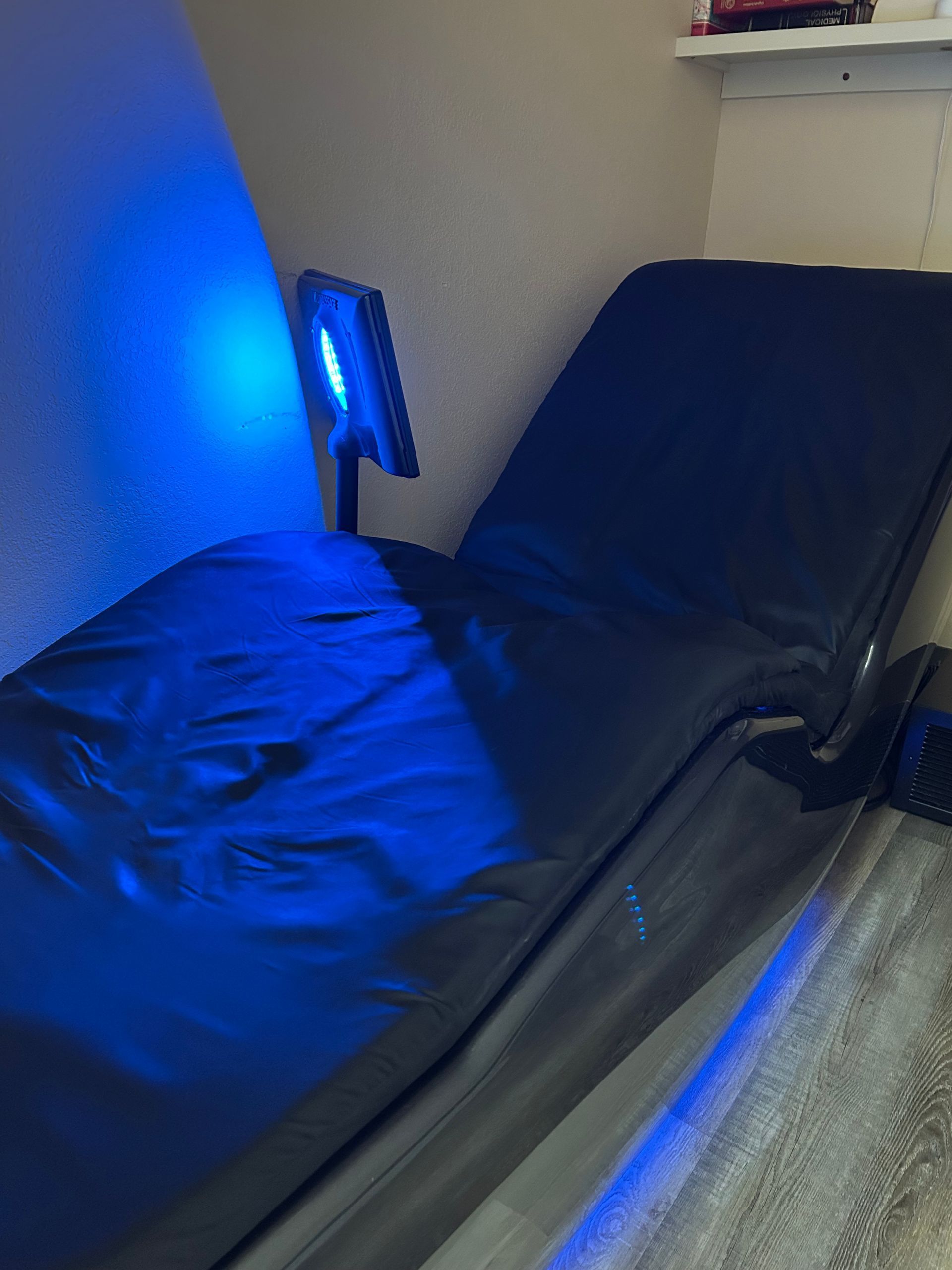 A blue light is shining on a black chair in a room.