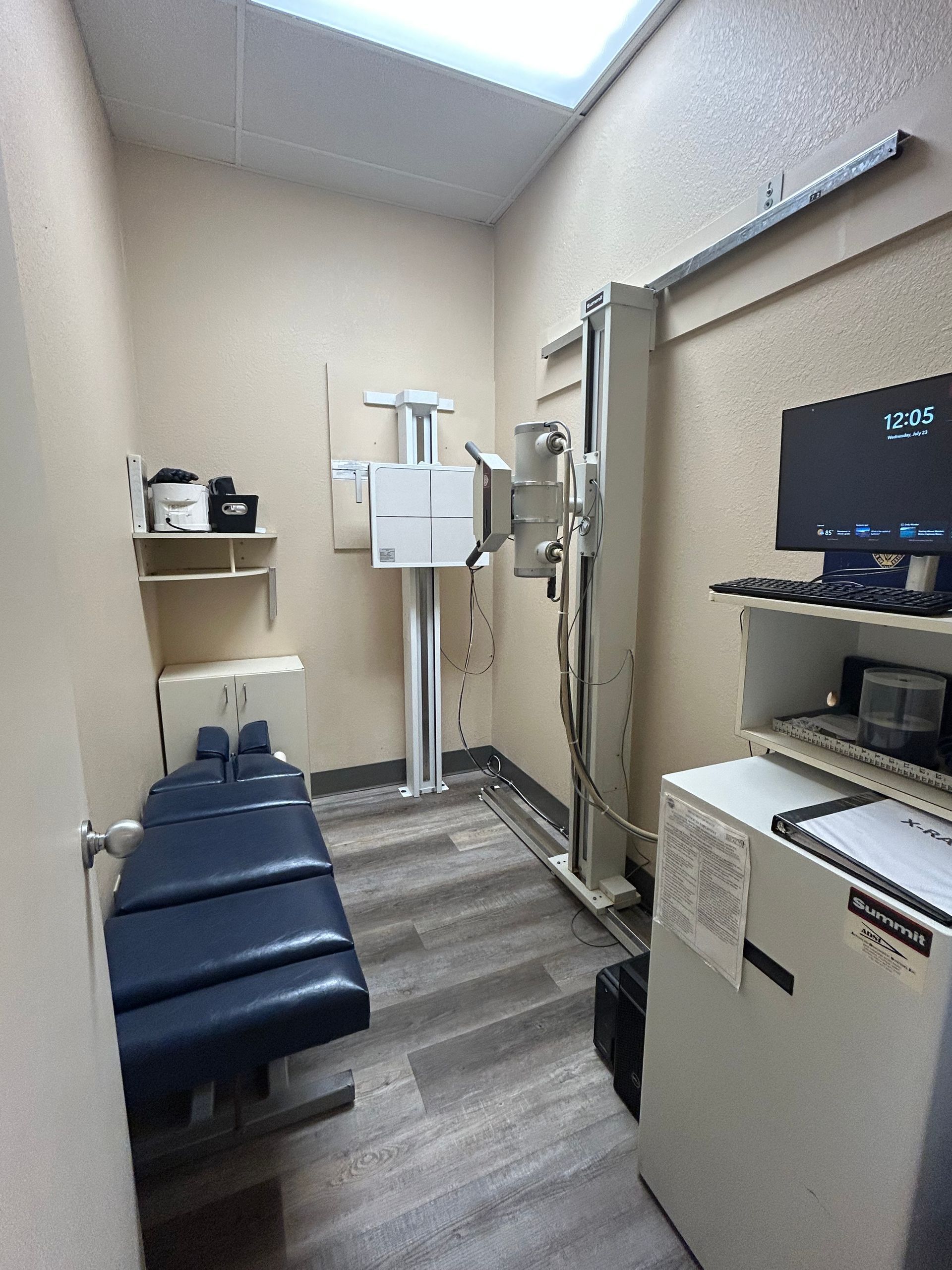 A room with a x-ray machine and a computer on the wall.