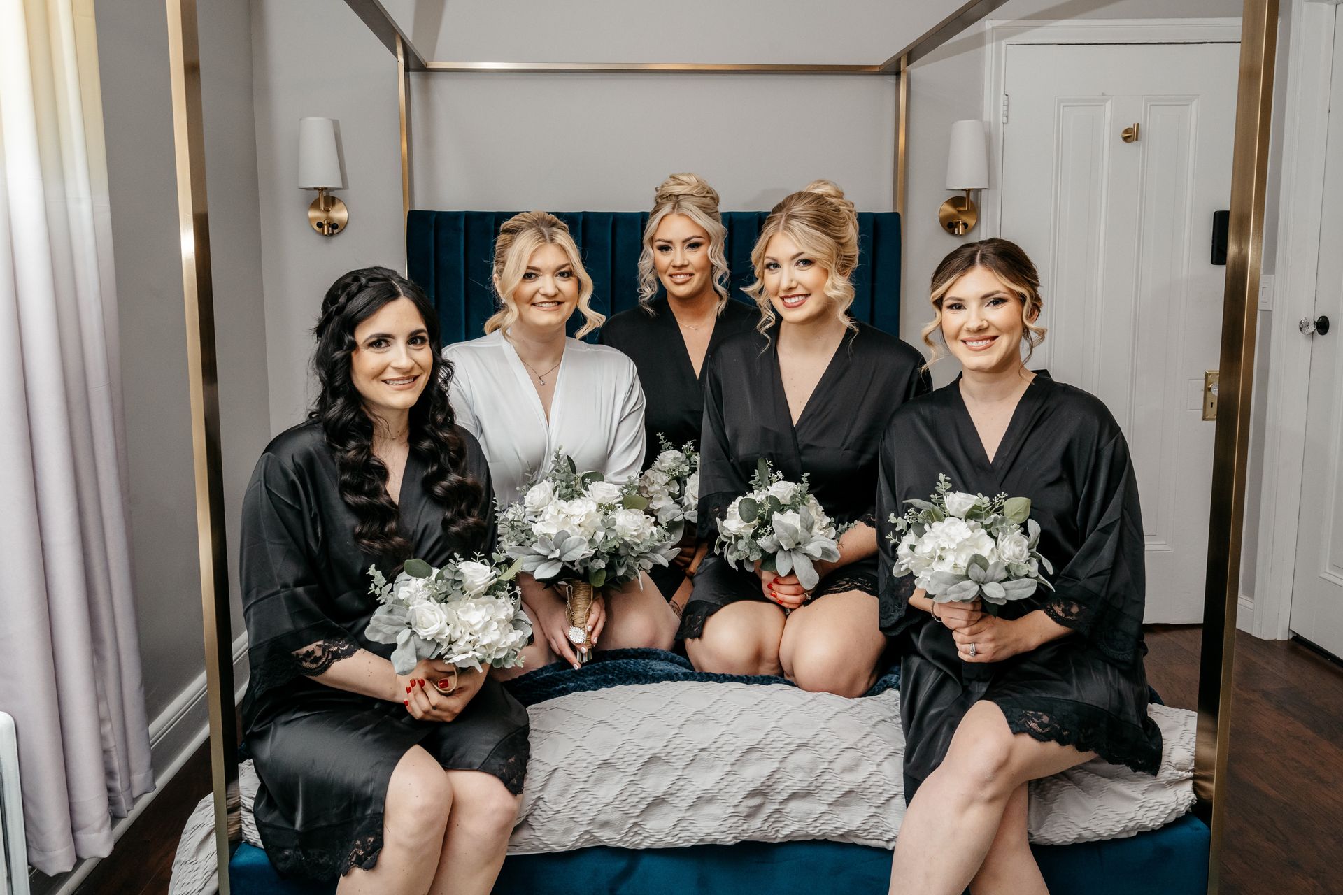 The bride and her bridesmaids are posing for a picture while sitting on a bed.