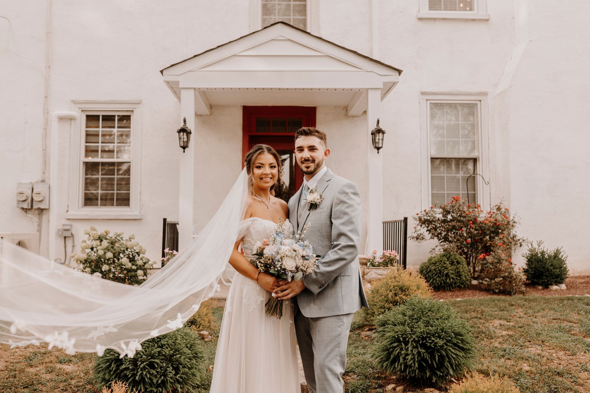 A bride and groom are posing for a picture in front of a white house.