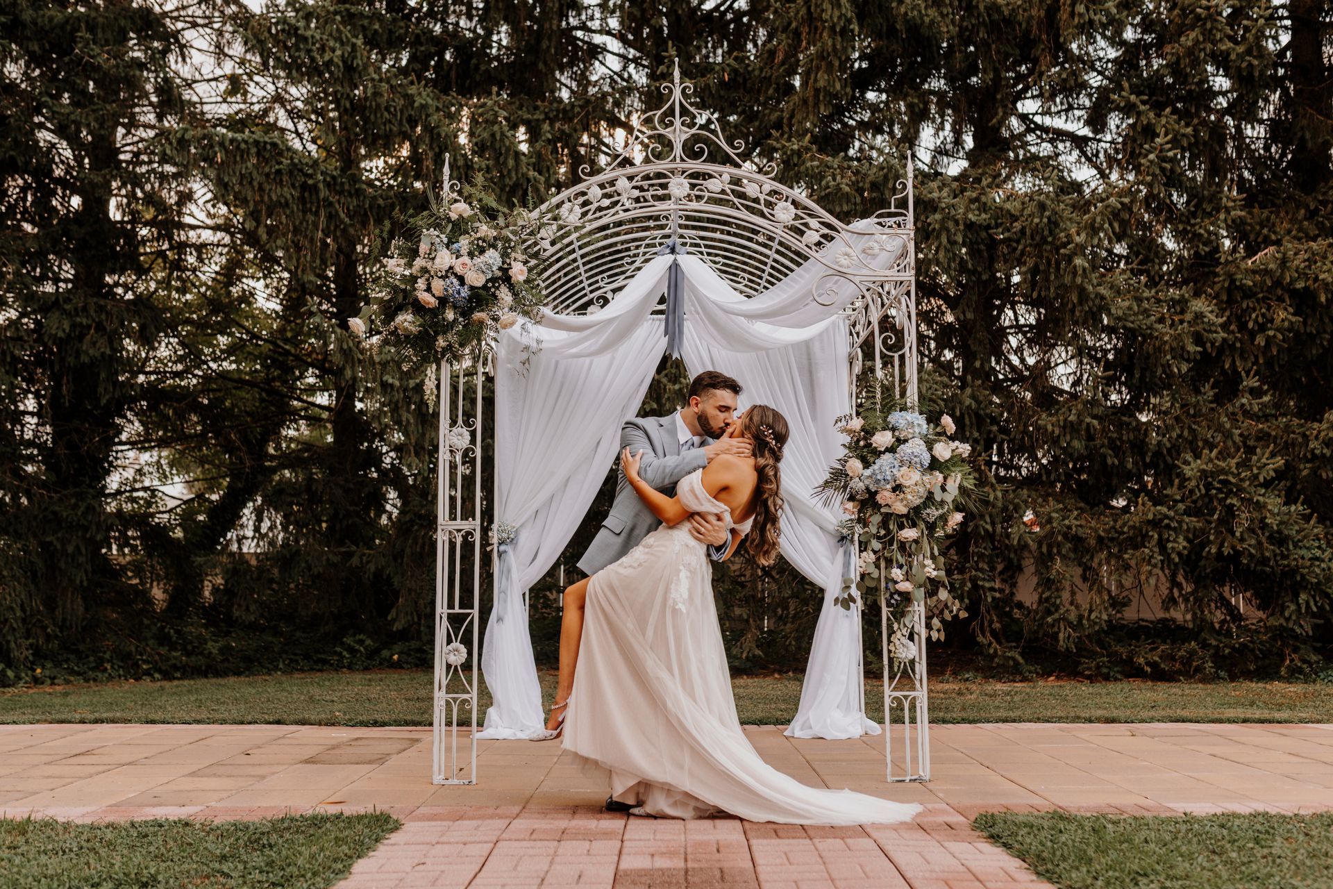 A bride and groom are kissing under a gazebo at their wedding.