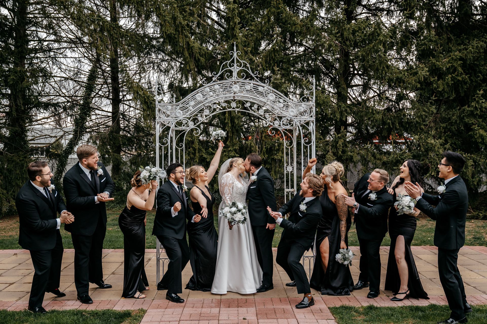 A bride and groom are kissing in front of their wedding party.