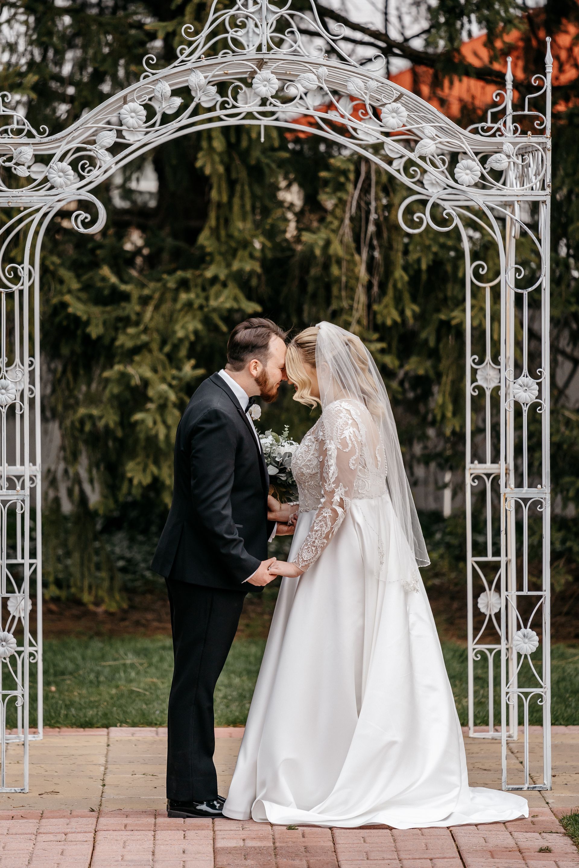 A bride and groom are kissing under a white archway.