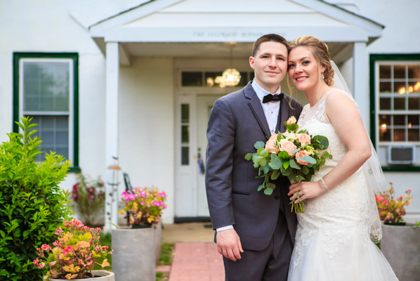 A bride and groom are posing for a picture in front of a white house.