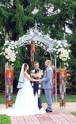 A bride and groom are holding hands during their wedding ceremony under an arch.