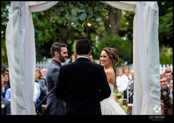 A bride and groom are smiling at each other during their wedding ceremony.