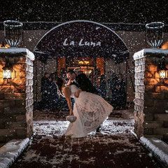 A bride and groom are kissing in the snow in front of a building.