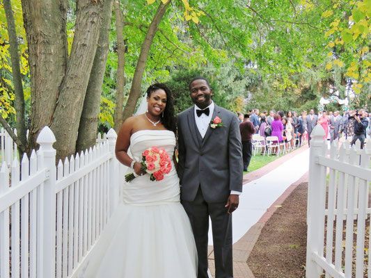 A bride and groom are posing for a picture in front of a white picket fence.