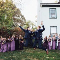 A bride and groom are jumping in the air in front of their wedding party.