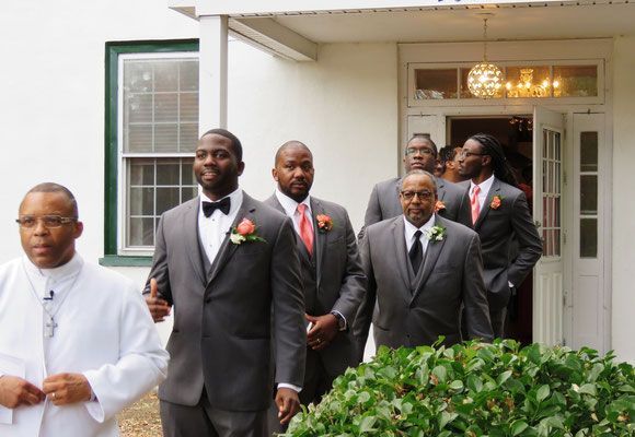 A group of men in suits and ties are walking in front of a white building.