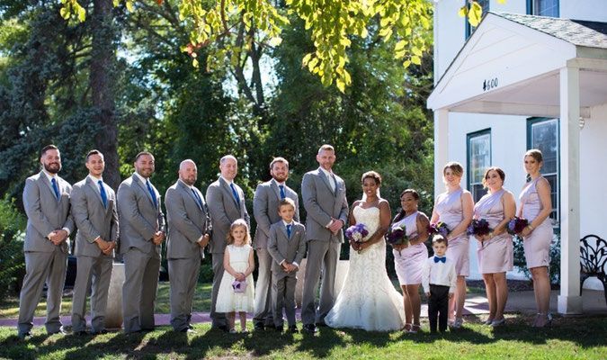 A bride and groom pose with their wedding party in front of a white house.