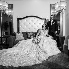 A bride and groom are posing for a black and white photo in front of a bed.