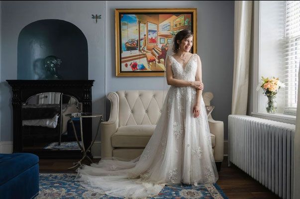 A woman in a wedding dress is standing in a living room next to a couch.