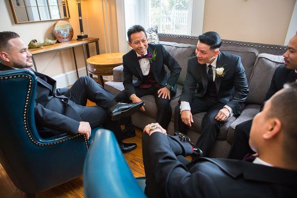 A group of men in suits are sitting around a couch in a living room.