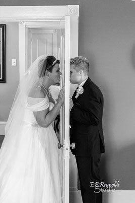 A bride and groom are kissing through a door.