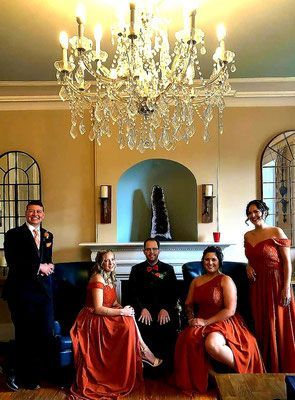 A group of people are posing for a picture in a living room under a chandelier.