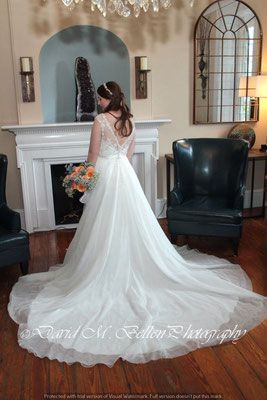 A bride in a wedding dress is standing in front of a fireplace holding a bouquet of flowers.
