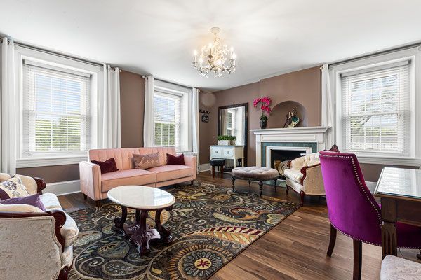 A living room with a pink couch , purple chairs , and a fireplace.