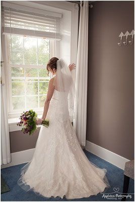 A bride in a wedding dress is standing in front of a window holding a bouquet of flowers.