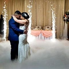 A bride and groom are dancing in the fog at their wedding reception.