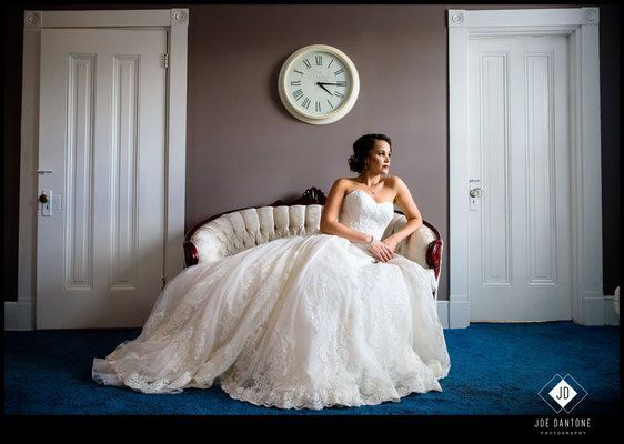 A woman in a wedding dress is sitting on a couch in front of a clock.