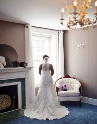 A bride in a wedding dress is standing in front of a fireplace in a room.