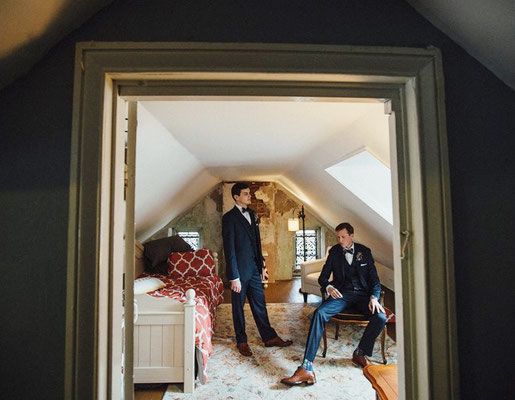 Two men in suits are standing next to each other in an attic room.