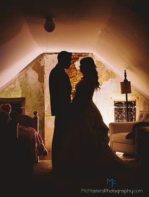 A bride and groom are standing in an attic looking at each other.