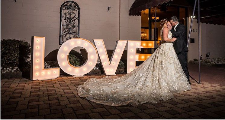 A bride and groom are kissing in front of a large love sign.