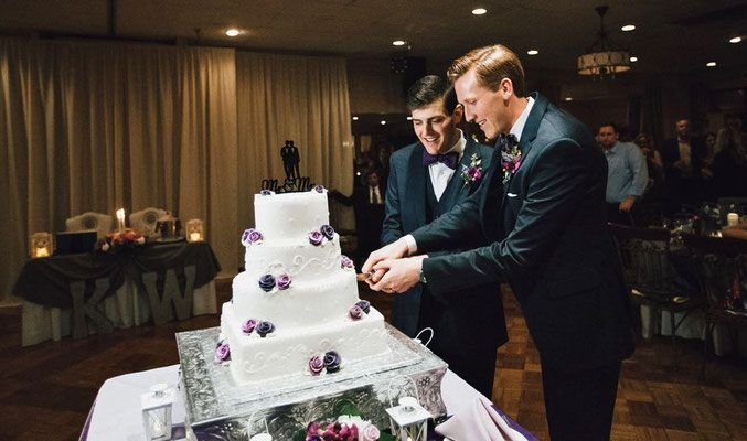 Two men are cutting a wedding cake on a table.